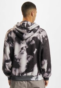 Hooded sweatshirt v črni in sivi tie-dye vzorcu, narejen iz mehkega blaga. Ima sprednji žep ter rebraste manšete in rob.