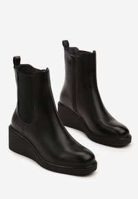 Bottines à talon compensé en cuir noir avec des panneaux élastiques sur les côtés et une languette à l'arrière, offrant une texture lisse et un design à bout rond.