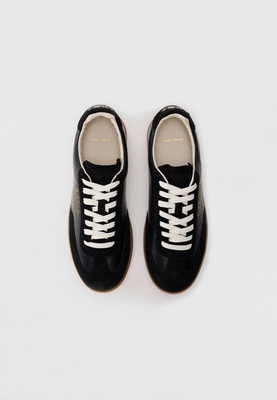 Un paio di sneakers nere con lacci bianchi, suole in gomma e fodera interna beige, posizionate affiancate su uno sfondo bianco.