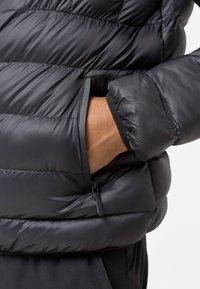 Čierna prešívaná bunda vyrobená z hladkej, lesklej látky s horizontálnym prešívaním. Obsahuje bočnú vrecko na zips a elastické manžety.