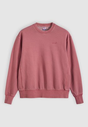 Rožinės spalvos džemperis, pagamintas iš minkšto medvilnės audinio, su apvalia iškirpte, ilgomis rankovėmis ir subtilia krūtinės logotipu. Švelnios tekstūros.