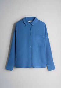 Cămașă albastră cu mâneci lungi, cu nasturi și guler, având un buzunar la piept, prezentată așezată pe un fundal gri deschis.