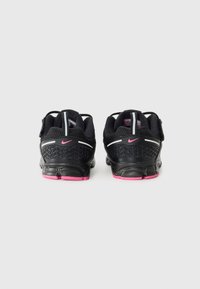 Scarpe da ginnastica nere con un design testurizzato, accenti rosa sulla suola, strisce riflettenti e dettagli in rete sulla parte superiore.