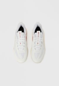 Scarpe da ginnastica bianche con materiale in mesh, design testurizzato, forma arrotondata e accenti rossi. Allacciatura e colli imbottiti offrono supporto.