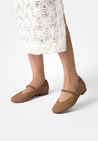 Hnědé semišové balerínky se zaoblenou �špičkou a dekorativním páskem přes nárt, s malým nízkým podpatkem a hladkou texturou.