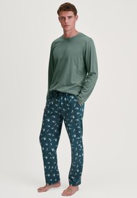 Heren pyjama top met lange mouwen in het groen, gecombineerd met marineblauwe pyjamabroek met een patroon van kleine vogelontwerpen, gemaakt van zachte, lichte stof.