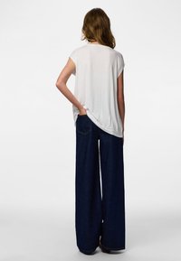 Fehér rövid ujjú felső széles szárú sötétkék farmernadrággal; sima anyag, laza szabás, finom hátul található szegély részletekkel.