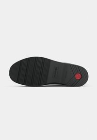 Talpă de pantof din cauciuc negru cu textură nervurată, având un logo de marcă și un accent roșu circular. Design plat, vârf curbat și nervuri adânci pentru aderență.