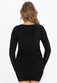Rochie neagră cu mânecă lungă, cu o textură pufoasă, având accente asemănătoare perlelor pe mâneci și un decolteu rotund.