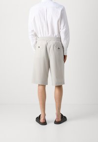 Shorts grigi chiaro con cintura elastica, due tasche posteriori con bottoni neri, abbinati a una camicia bianca con bottoni e sandali neri.