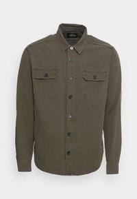 Camisa verde oliva de algodón con botones, que presenta un cuello clásico, dos bolsillos en el pecho y botones negros. Textura suave y corte recto.