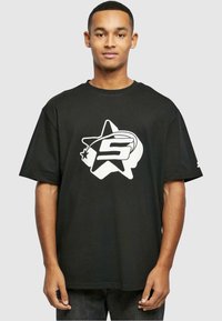 Sort bomulds t-shirt med en stor hvid stjerne og bogstavet "S" i midten. Korte ærmer og afslappet pasform.