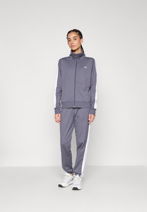 Chándal deportivo gris con chaqueta de cremallera y pantalones a juego. Presenta franjas laterales blancas. Está fabricado con un tejido suave y ligero.