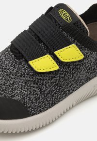 Czarne i szare dzianinowe sneakersy z dwoma żółtymi akcentami, elastycznymi paskami i teksturowaną podeszwą oraz gładką czarną osłoną palców.
