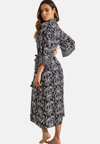 Lange marineblauwe ochtendjas met een wit en roest kleurig abstract patroon, klokmouwen en een strik taille, gemaakt van lichte stof.