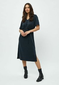 Dark green dress with short sleeves and a V-neckline, featuring a drawstring waist and side slits, paired with black ankle boots.
