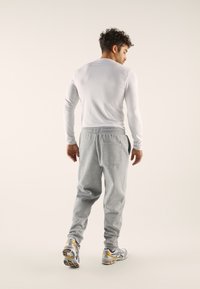 Gray fleece joggers with elastic waistband and back pocket, paired with a white long-sleeve top. Athletic shoes feature gray and yellow accents.