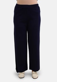 Navy wide-leg pants made of soft fabric, featuring an elastic waistband and laid-back fit. Paired with light-colored loafers.