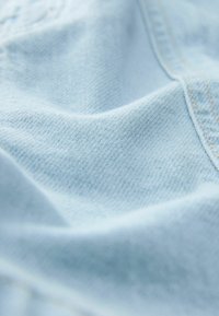 Tissu en coton bleu clair avec une surface douce et texturée, présentant de subtils motifs de tissage diagonal et un bord soigneusement piqué.