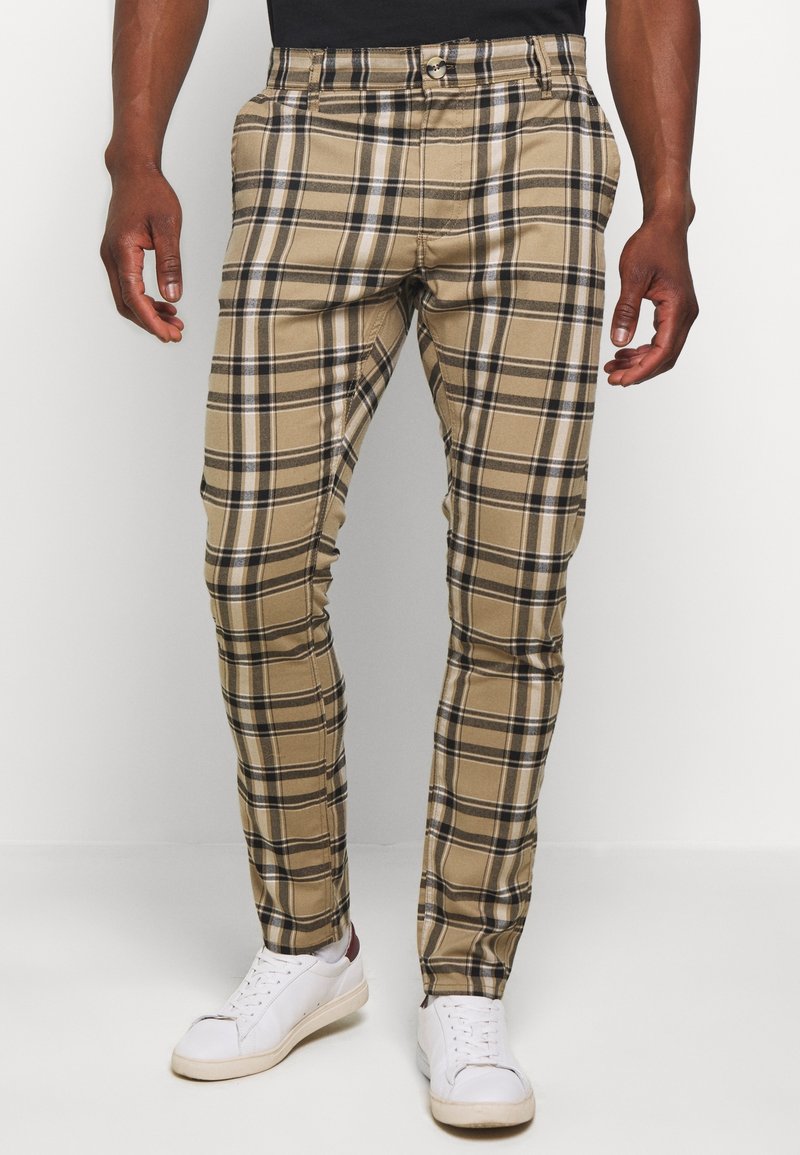 Beige plaid trousers made of cotton with black and white accents, featuring a fitted design and front pockets. Worn with white sneakers.