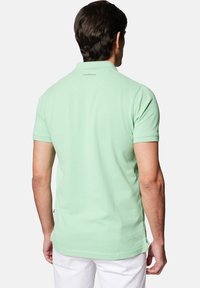 Miętowa koszulka polo z krótkim rękawem, wykonana z miękkiej bawełny, z klasycznym kołnierzykiem, bocznymi rozcięciami i małym logo na tylnej części dekoltu.
