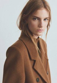 Bruine jas van een wolmix met een double-breasted ontwerp, brede revers en zwarte knopen. Gladde textuur en een getailleerde pasvorm.