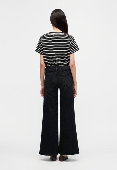 Μαύρο τζιν παντελόνι με φαρδιά μπάτζα, σε συνδυασμό με μαύρη και λευκή ριγέ μπλούζα. Η μπλούζα έχει κοντά μανίκια και άνετη εφαρμογή.