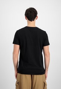 Juodas trumpas rankovė t-shirt su apvaliu kaklu, pagamintas iš lygios medžiagos, rodomas iš nugaros, derinamas su chaki spalvos kargo kelnėmis.