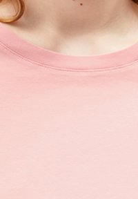 Ljusrosa t-shirt med rund hals. Tillverkad av mjukt, slätt tyg med en subtil textur. Inga synliga mönster eller designer.