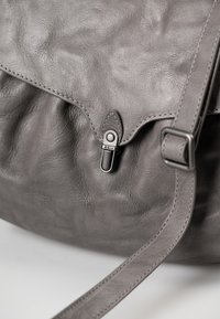 Borsa in pelle grigia con una superficie morbida e testurizzata. Presenta una chiusura a patta e una fibbia in metallo argentato, completata da una tracolla coordinata.