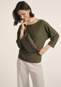 Brązowa torebka na ramię z wzorem, wykonana ze skóry, w kształcie zakrzywionym, z złotymi elementami i zapięciem na zamek, noszona na oliwkowej górze.