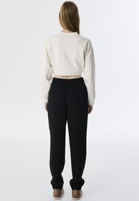 Sudadera crema cortada con mangas largas combinada con pantalones negros de cintura elástica que tienen bolsillos traseros, llevados con zapatos beige.