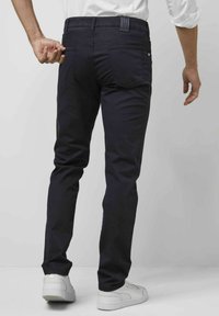 Pantalon bleu marine à coupe slim, doté de deux poches arrière et d'une étiquette logo discrète sur la taille. Texture de tissu lisse.