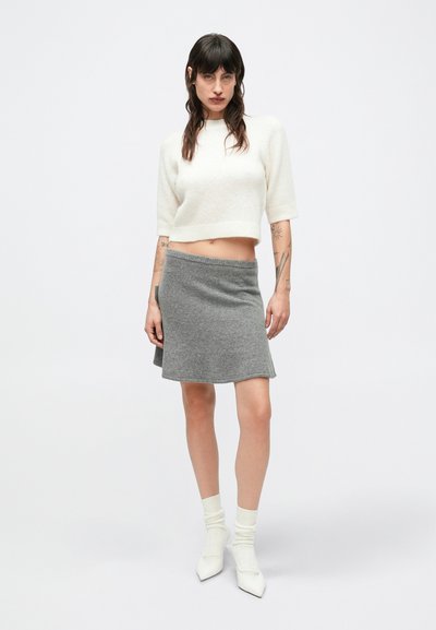 Κρεμ κοντό πουλόβερ, γκρι πλεκτή φούστα, λευκές κάλτσες αστραγάλου και λευκά μυτερά ψηλοτάκουνα. Απαλές υφές, εφαρμοστή γραμμή και καθαρές γραμμές.