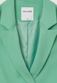 Grüner Blazer mit glatter Textur, ausgestattet mit einem Reverskragen und einem Innenfutter aus Satin. "CALLIOPE"-Label innen sichtbar. Größe: S.