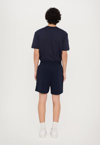 Navy bomulds t-shirt med korte ærmer parret med matchende shorts. Sættet har en elastisk talje og et enkelt design. Hvide sneakers bruges.