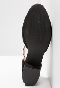 Chaussure en daim noir avec un bout fermé et un talon ouvert. La semelle est en caoutchouc noir texturé, embossée de la taille '37'.