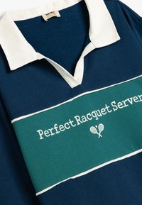 Polo navy con cuello blanco y banda horizontal verde. Presenta el texto "Perfect Racquet Server" y dos iconos de raquetas cruzadas.