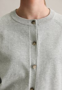 Grå stickad cardigan med rund halsringning, fem knappar fram och raglanärmar med en mjuk textur.