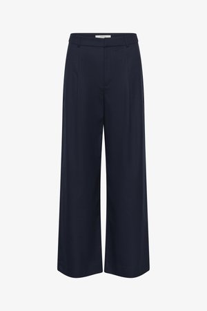 Tumši zili, platām kājām brīvs audums bikses. Tās ir ar augstu jostasvietu, priekšējiem krokām un sānu kabatām. Šūtas ar tīrām līnijām un piegriezumu.