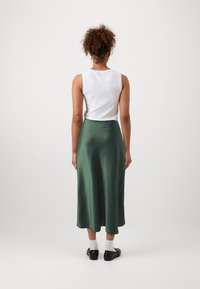 Fustă midi din satin verde, cu o textură fină, asortată cu un top alb fără mâneci, purtată cu pantofi negri și șosete albe.