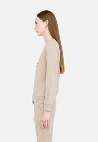 Felpa beige con maniche lunghe e polsini a coste, dal morbido aspetto e con scollo a giro. Abbinata a pantaloni beige coordinati.