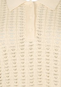 Gebreide polo in zacht beige, met een textuur van een bladpatroon, drie knopen en een ribgebreide kraag voor extra detail.