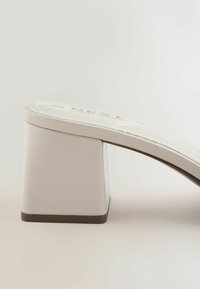 Sandale mule blanche à bout ouvert avec un talon bloc et une semelle matelassée sur un fond uni.