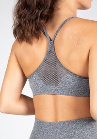 Sujeción deportiva gris con diseño de espalda cruzada que cuenta con un inserto de malla. El material es texturizado y el ajuste general es ceñido y de soporte.