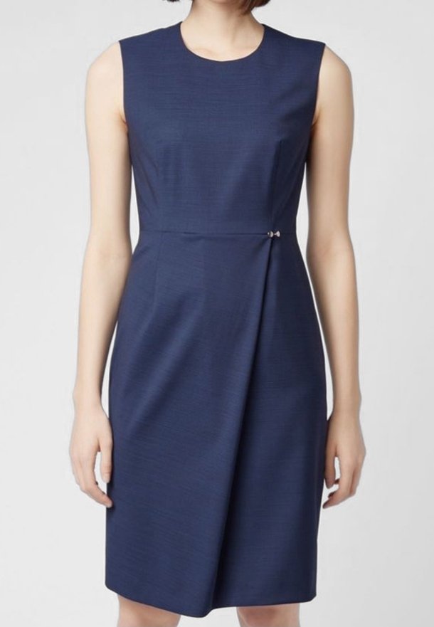 Robe sans manches bleu marine longueur genou avec un col rond et une petite agrafe décorative à la taille, créant un léger drapé.