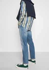 Koszula w kratę w odcieniach niebieskiego, zielonego i żółtego; granatowa bluza narzucona; jasnoniebieskie dżinsy; zielone trampki z białymi zdobieniami.