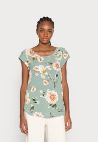 Blusa floral de manga curta em verde claro, com grandes flores laranjas e brancas, decote barco e corte descontraído. Tecido suave com textura lisa.