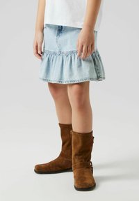Jupe en denim à volants de couleur bleu clair avec un ourlet froncé. Associée à des bottes en daim marron montantes avec une fermeture éclair sur le côté et des détails de sangle.