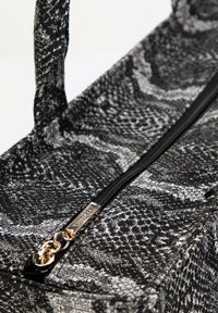 Sac au motif serpent noir et blanc avec une finition en tissu lisse, doté d'un tirette en or et d'un tag de marque.